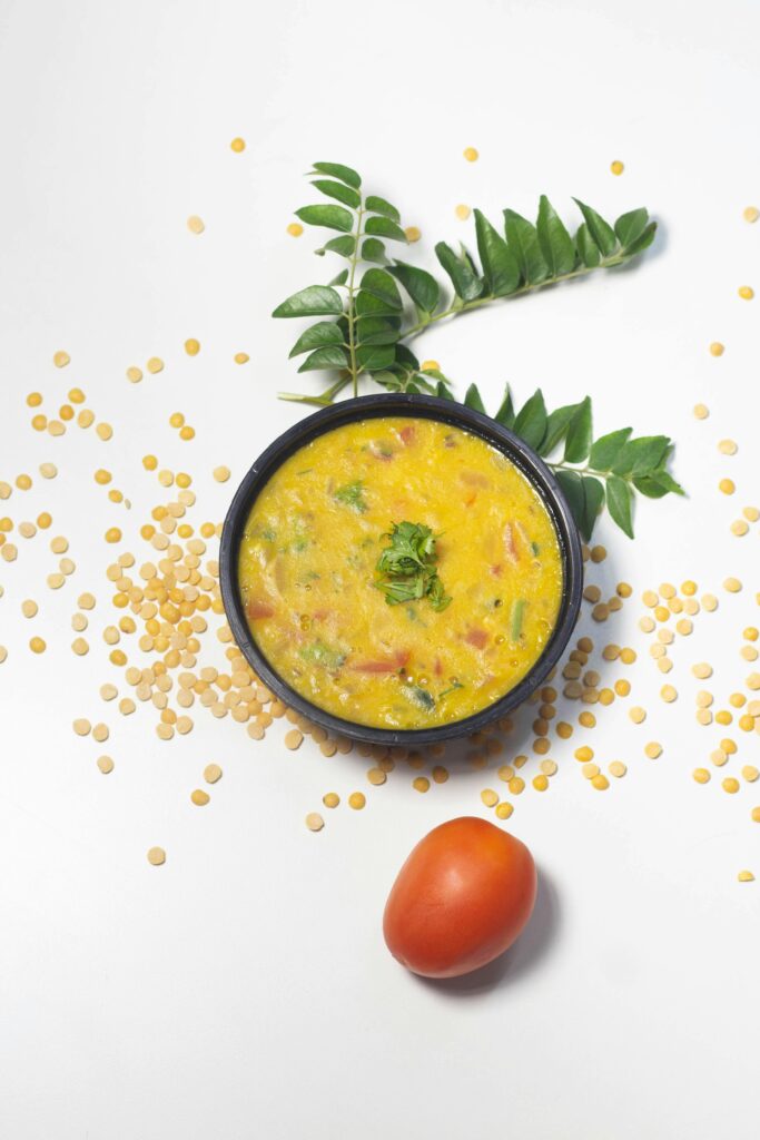 Mouthwatering Indian yellow lentil soup garnished with herbs, served with tomatoes and curry leaves.
